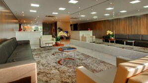 A modern lobby with a grey sofa, a coffee table, and a reception desk. - Brisa Tower Hotel (Ceilandia)