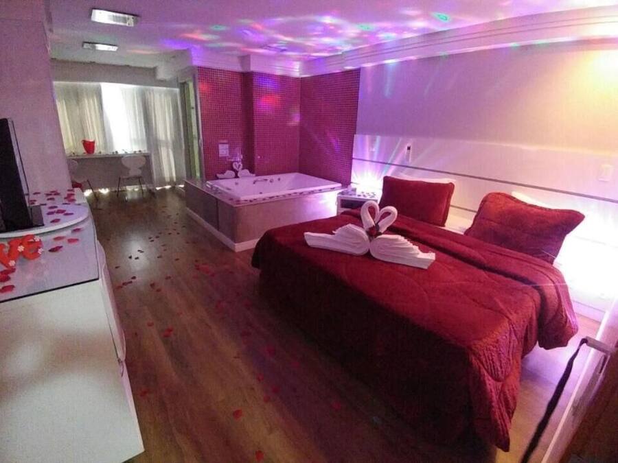 Une chambre d’hôtel avec une couvre-lit rouge, une grande fenêtre et un jacuzzi.