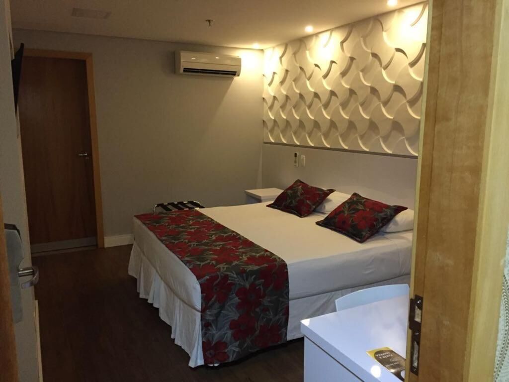 Una habitación de hotel con una cama, una mesita de noche, un equipo de aire acondicionado y una pared con diseño.