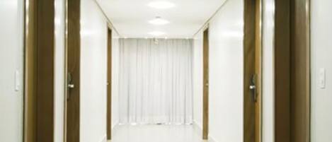 Um corredor comprido e estreito, com paredes brancas e portas de ambos os lados.