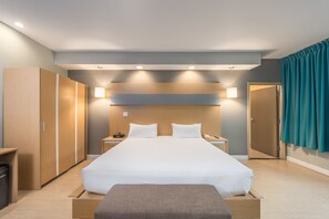A modern hotel room with a large bed, bedside tables, a wardrobe, and a bathroom door. - Royal Oasis (Petionville)