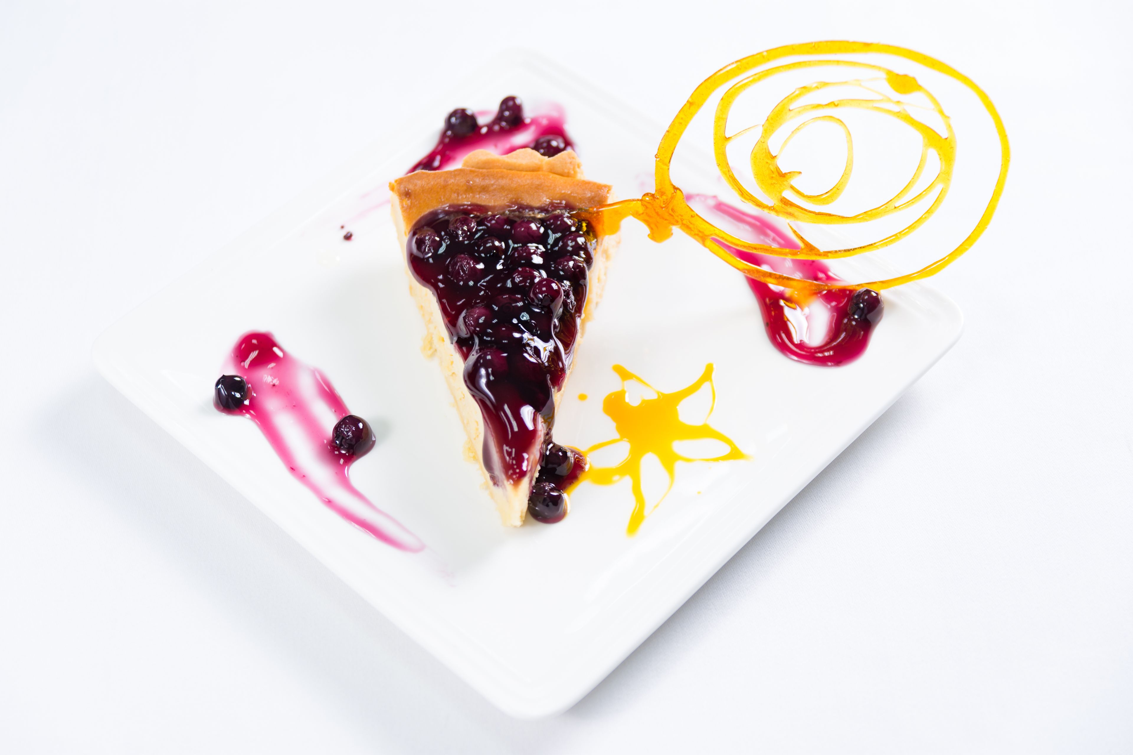 A slice of pie with a decorative yellow swirl and berry sauce on a white plate.