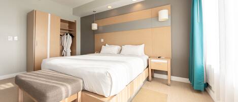 Una habitación de hotel moderna con una cama grande, un armario de madera, una mesita de noche y un banco.