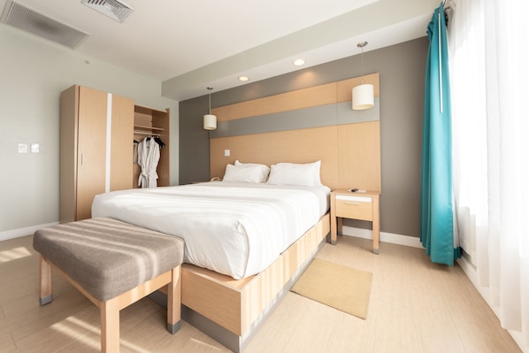 Una habitación de hotel moderna con una cama grande, un armario de madera, una mesita de noche y un banco.