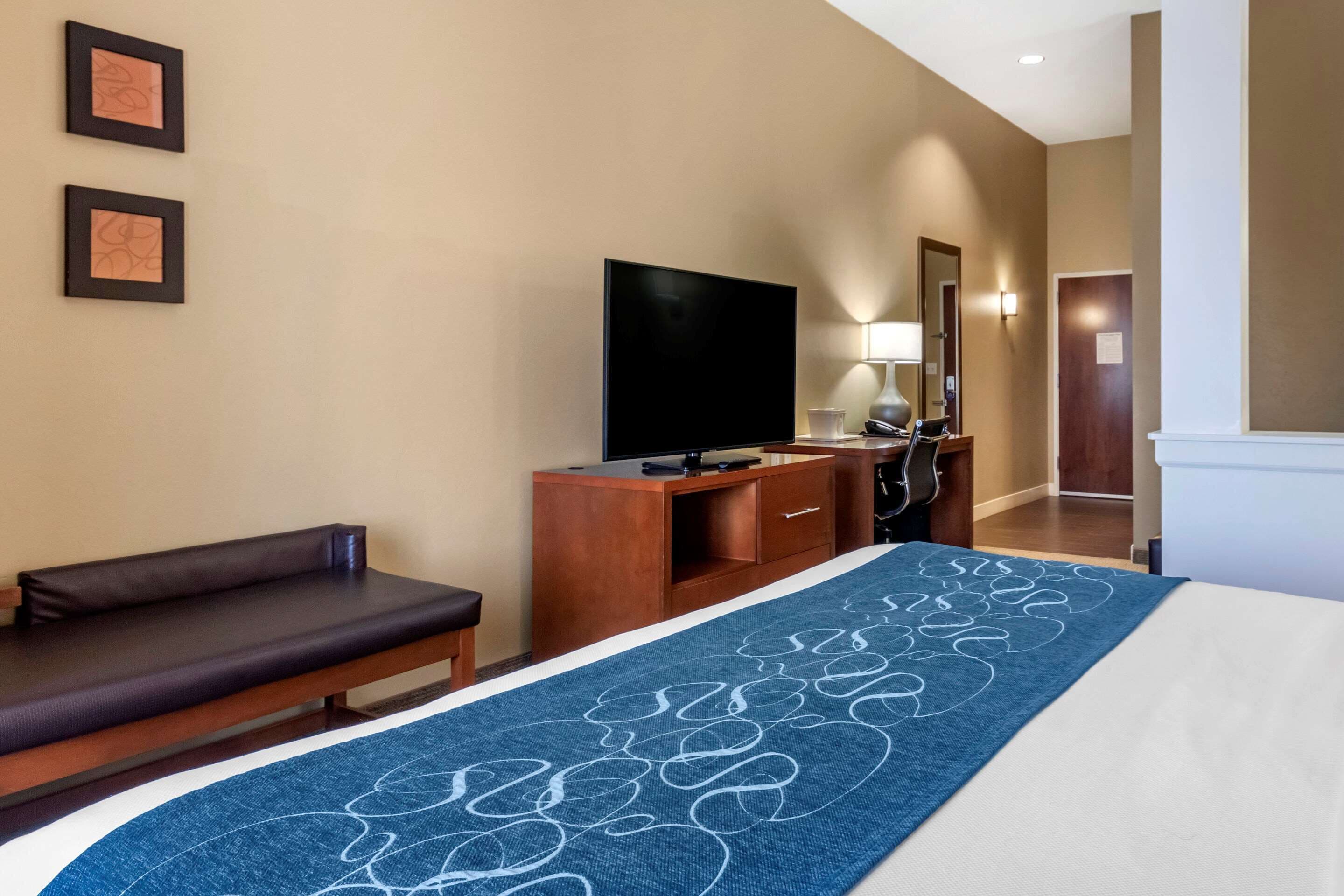 A hotel room with a bed, a bench, a TV, a desk, and a mirror.