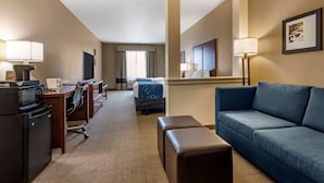 Habitación de hotel con escritorio, silla de oficina, sofá y cama con cabecera azul.