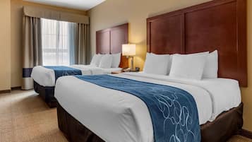 Una habitación de hotel con dos camas, un gran cabecero de madera, una mesita de noche con lámpara y una ventana con cortinas.