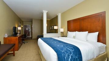 A hotel room with a large bed, a desk with a computer, a chair, and a lamp.