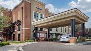 Un hotel Comfort Suites con entrada cubierta, fachada de ladrillo y un automóvil estacionado frente.