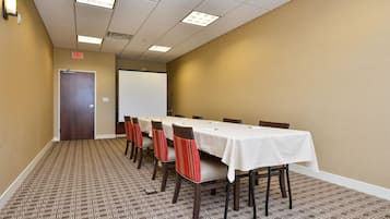 A conference room with a long table, chairs, a projector screen, and an exit door.