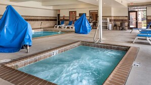 Un área de piscina hotelera con dos jacuzzis, sillones de descanso y una zona de estar cubierta.