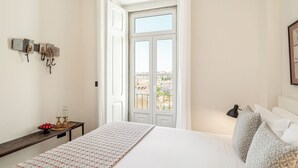 Un dormitorio con cama, mesita de noche con lámpara, ventana con vistas y perchero en la pared.