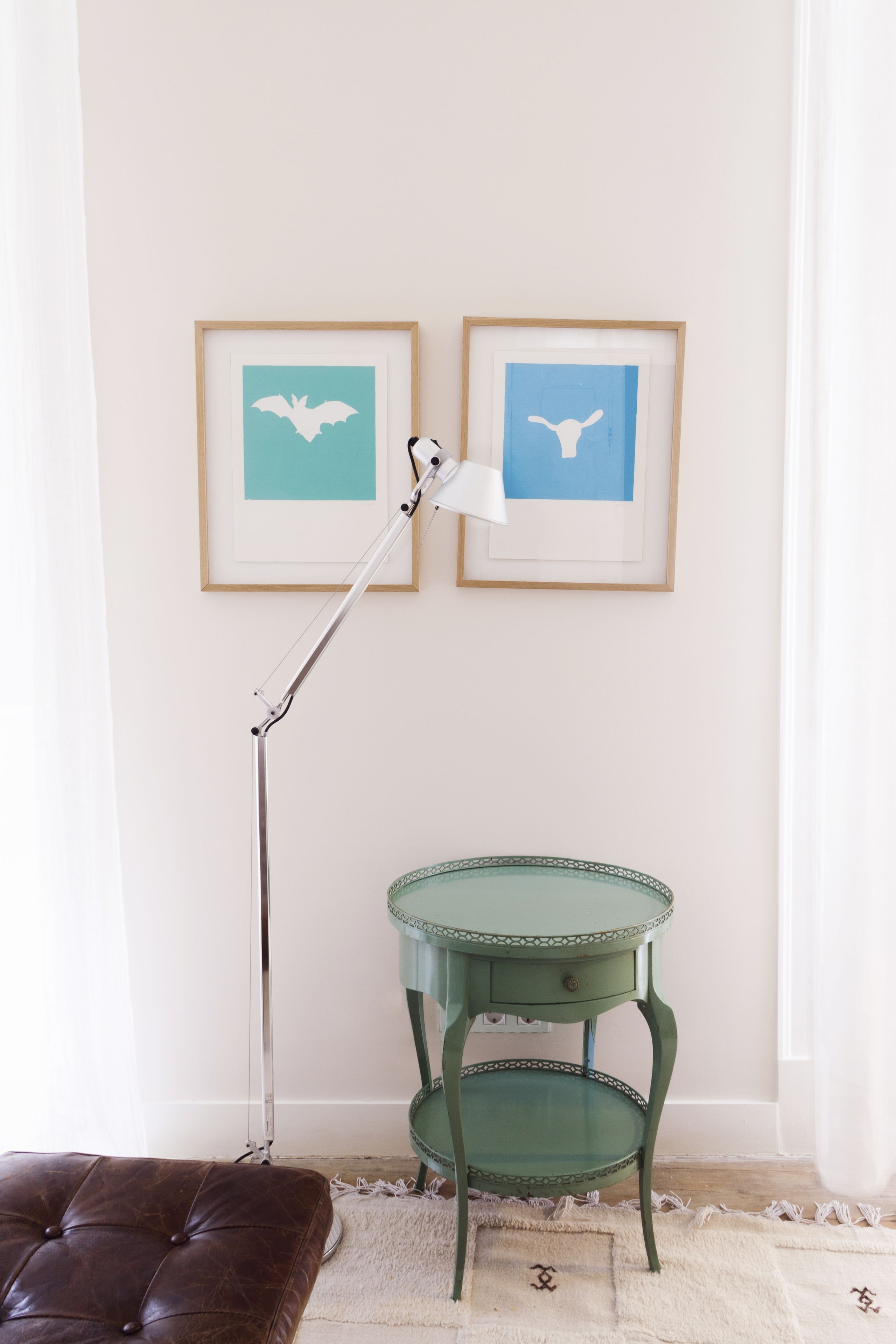 Una habitación con una mesita auxiliar verde, un otoman de cuero marrón y dos obras de arte enmarcadas que muestran murciélagos.