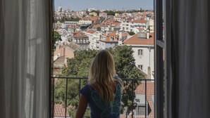 Una persona sentada en un balcón con vistas a un paisaje urbano con edificios y cielo despejado.