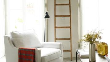 Una sala de estar con un sillón blanco, un reposapiés negro, una escalera de madera, una lámpara de pie y una mesa de centro con libros.