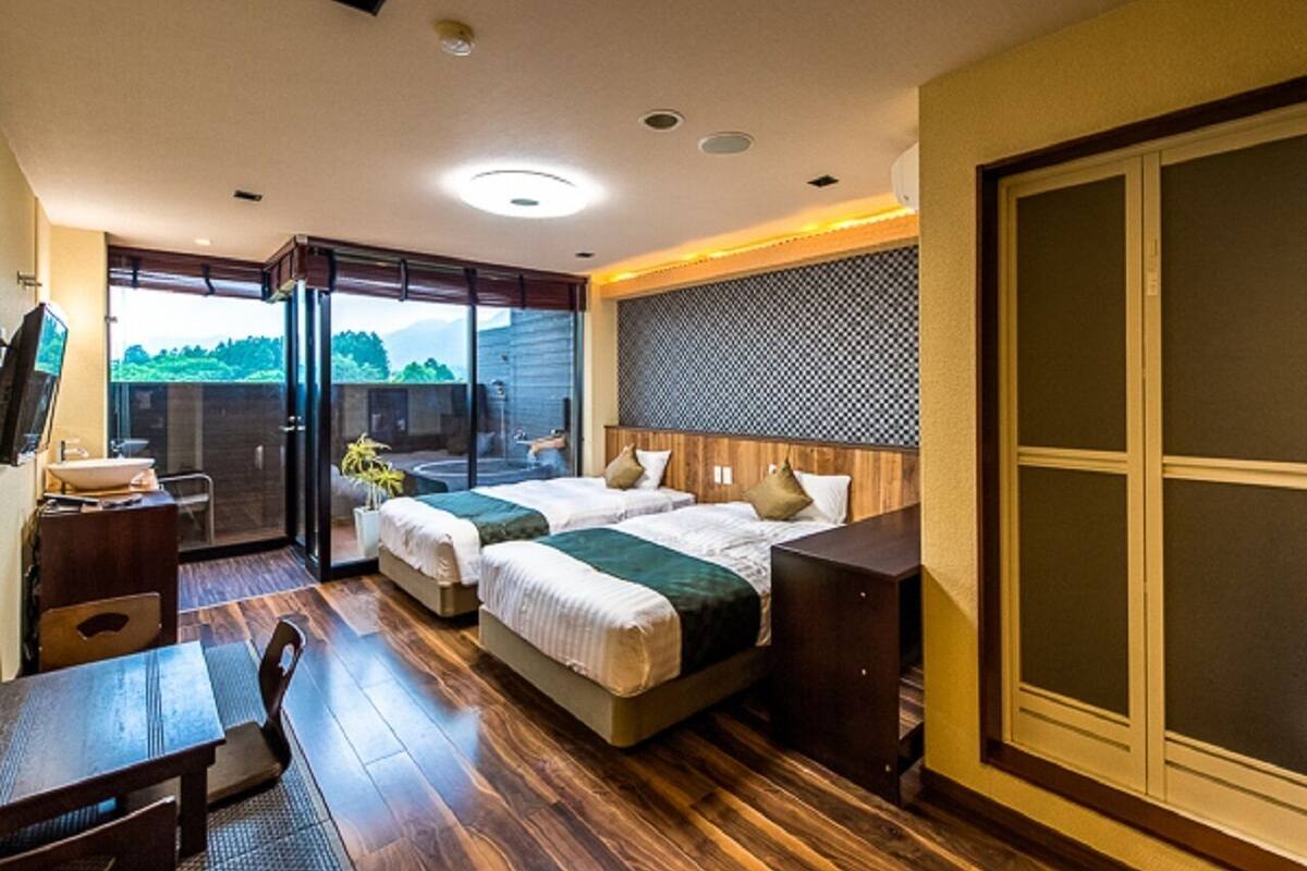 A modern hotel room with a balcony, two beds, a desk, and a large sliding door.