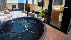 Habitación de hotel moderna con una gran fuente de agua negra, una zona de estar acogedora con sofá y sillones, una pequeña mesa de comedor y vistas al cielo a través de amplias ventanas.