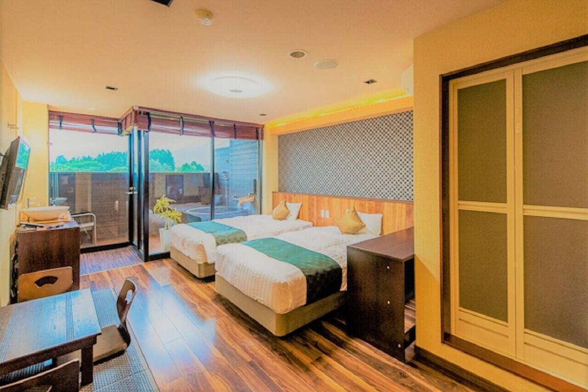 A hotel room with two beds, a desk, and a balcony with a view.