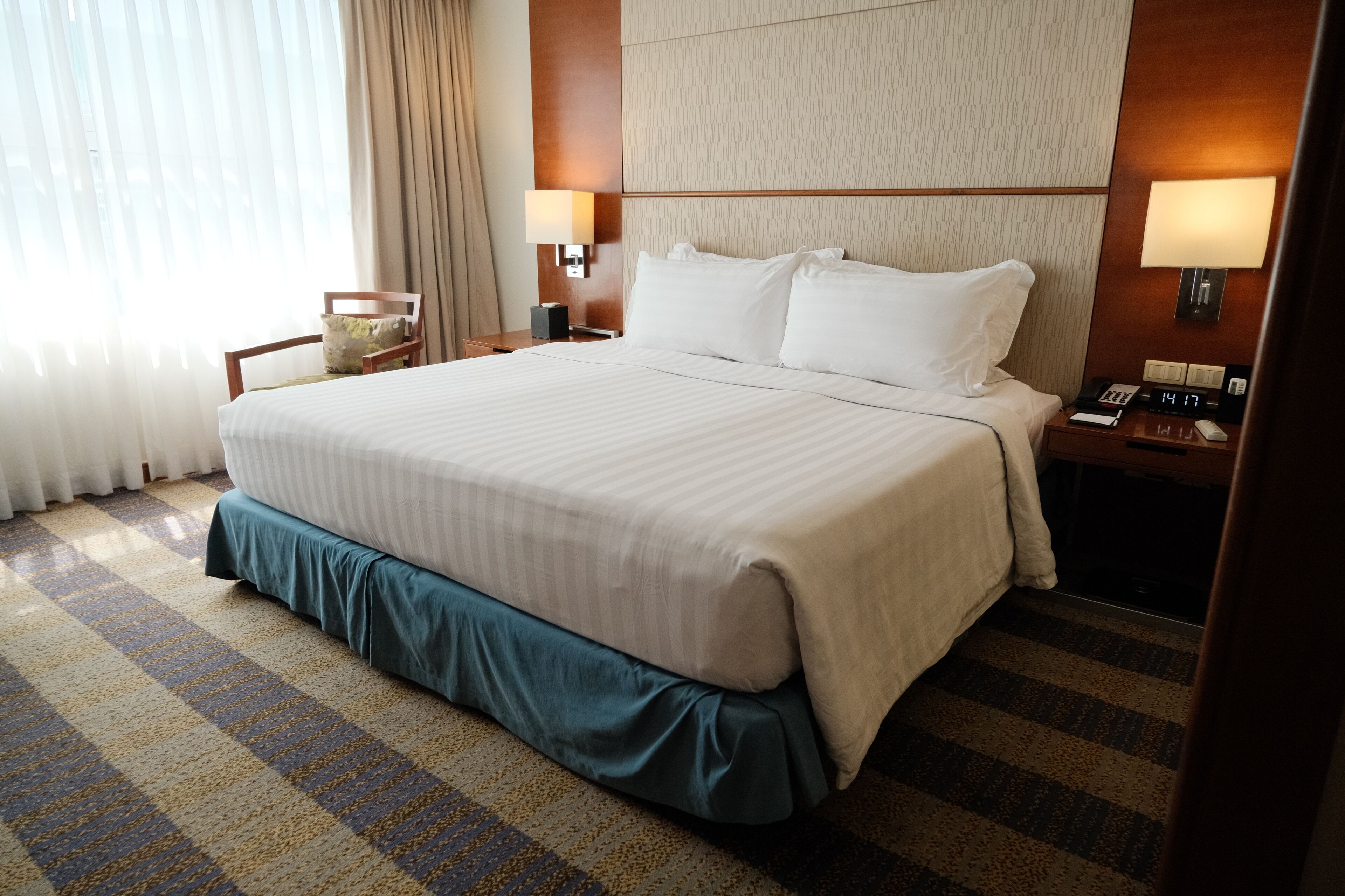 Habitación de hotel con una cama grande, dos mesitas de noche, una silla y una ventana con cortinas.
