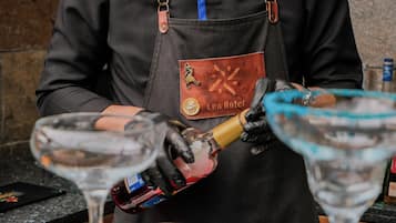 A person in a black apron with a badge, pouring a drink into a martini glass.