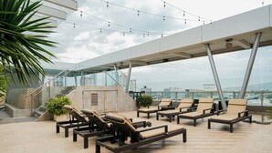 Un área de lounge en la azotea con tumbonas, plantas en macetas y vistas de la ciudad.