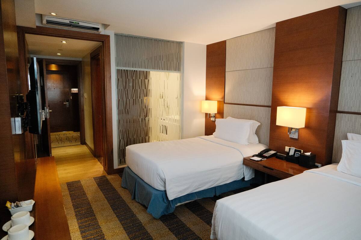 A hotel room with two beds, a desk, a telephone, and a lamp.