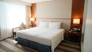 Une chambre d’hôtel avec un grand lit, deux tables de chevet avec des lampes, une chaise et une petite table de nuit avec une horloge.