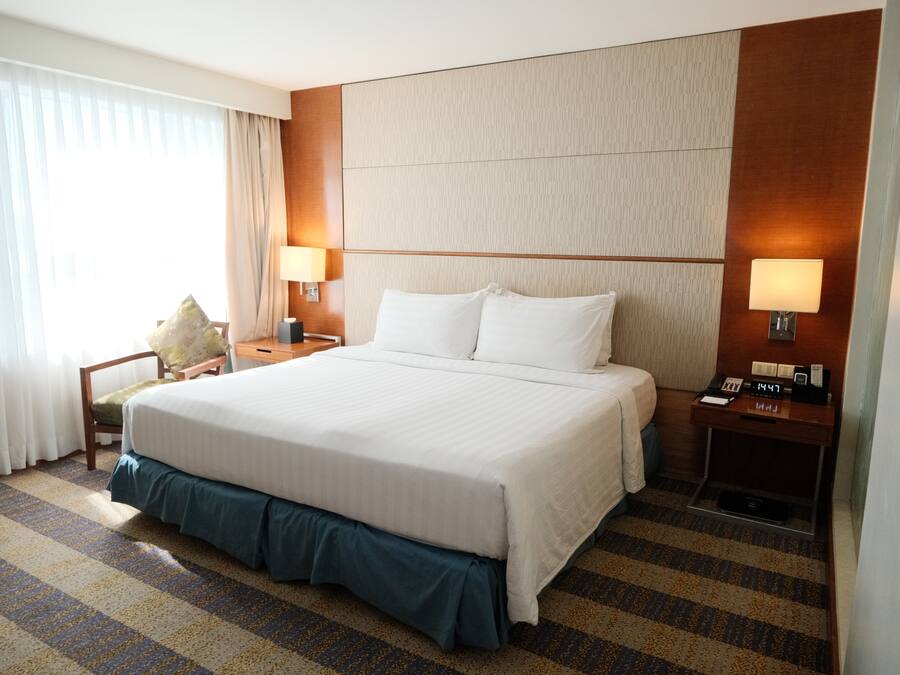 Une chambre d’hôtel avec un grand lit, deux tables de chevet avec des lampes, une chaise et une petite table de nuit avec une horloge.