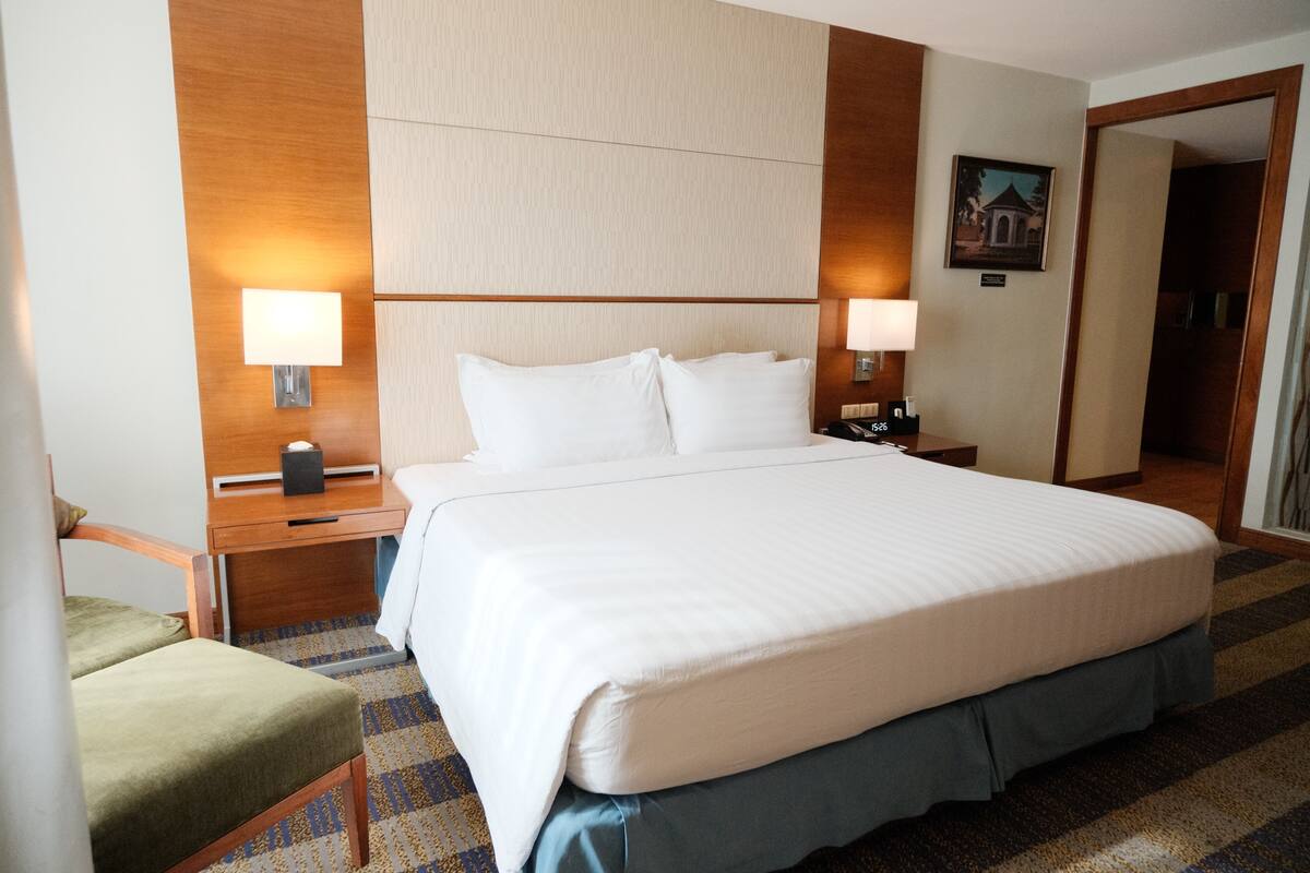 A hotel room with a large bed, two bedside tables with lamps, a chair, and a wooden headboard.