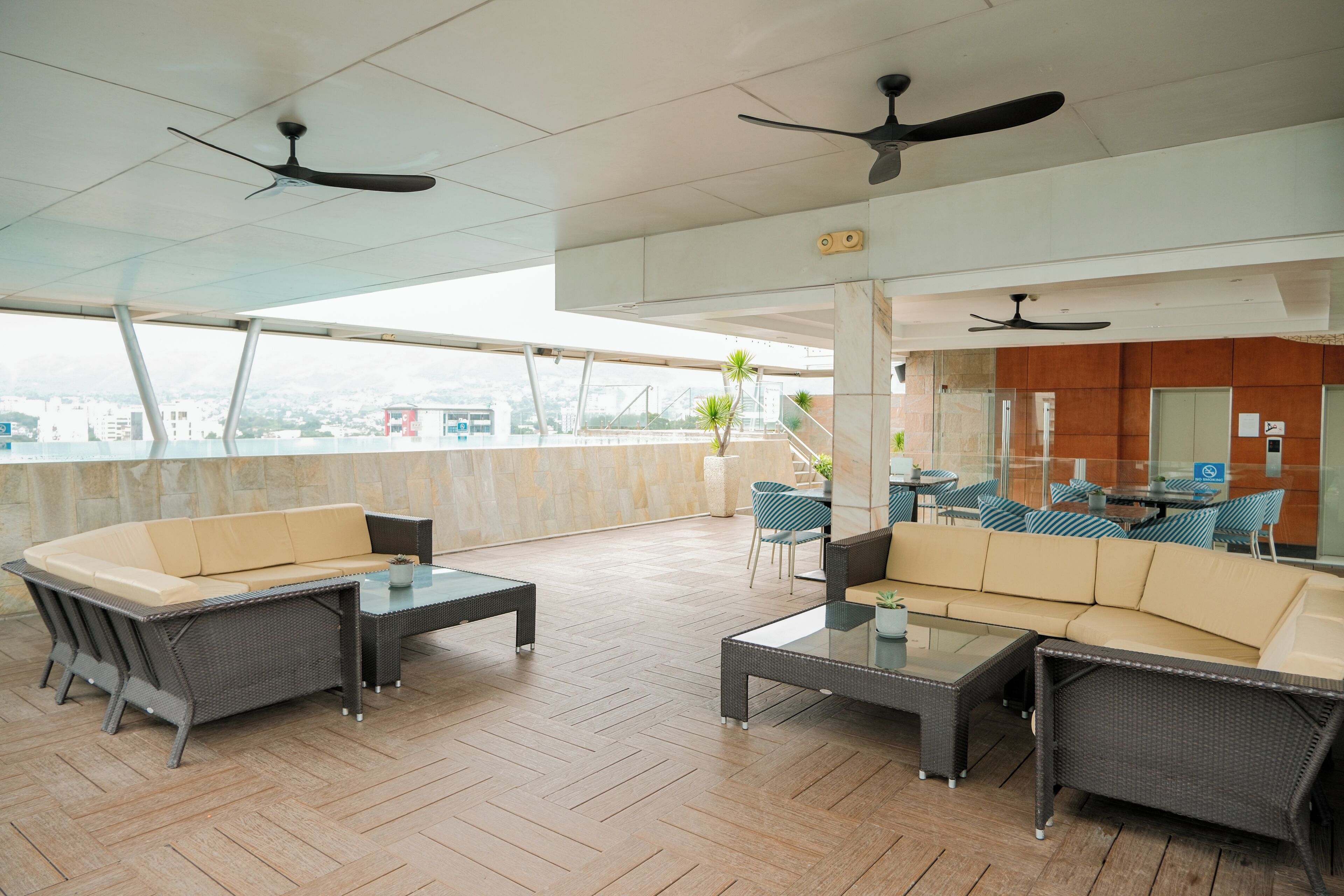 An outdoor seating area with wicker furniture, ceiling fans, and a view of the city.