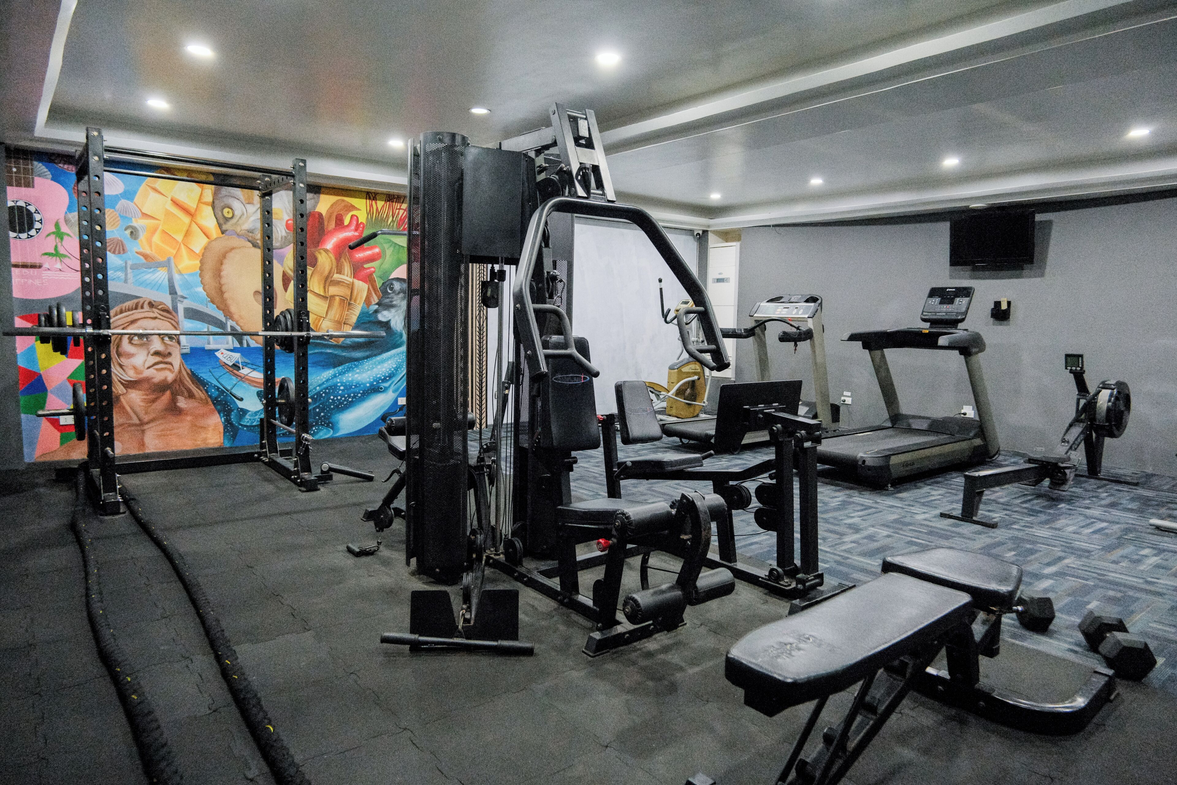 A gym with exercise equipment, a treadmill, and a mural on the wall.