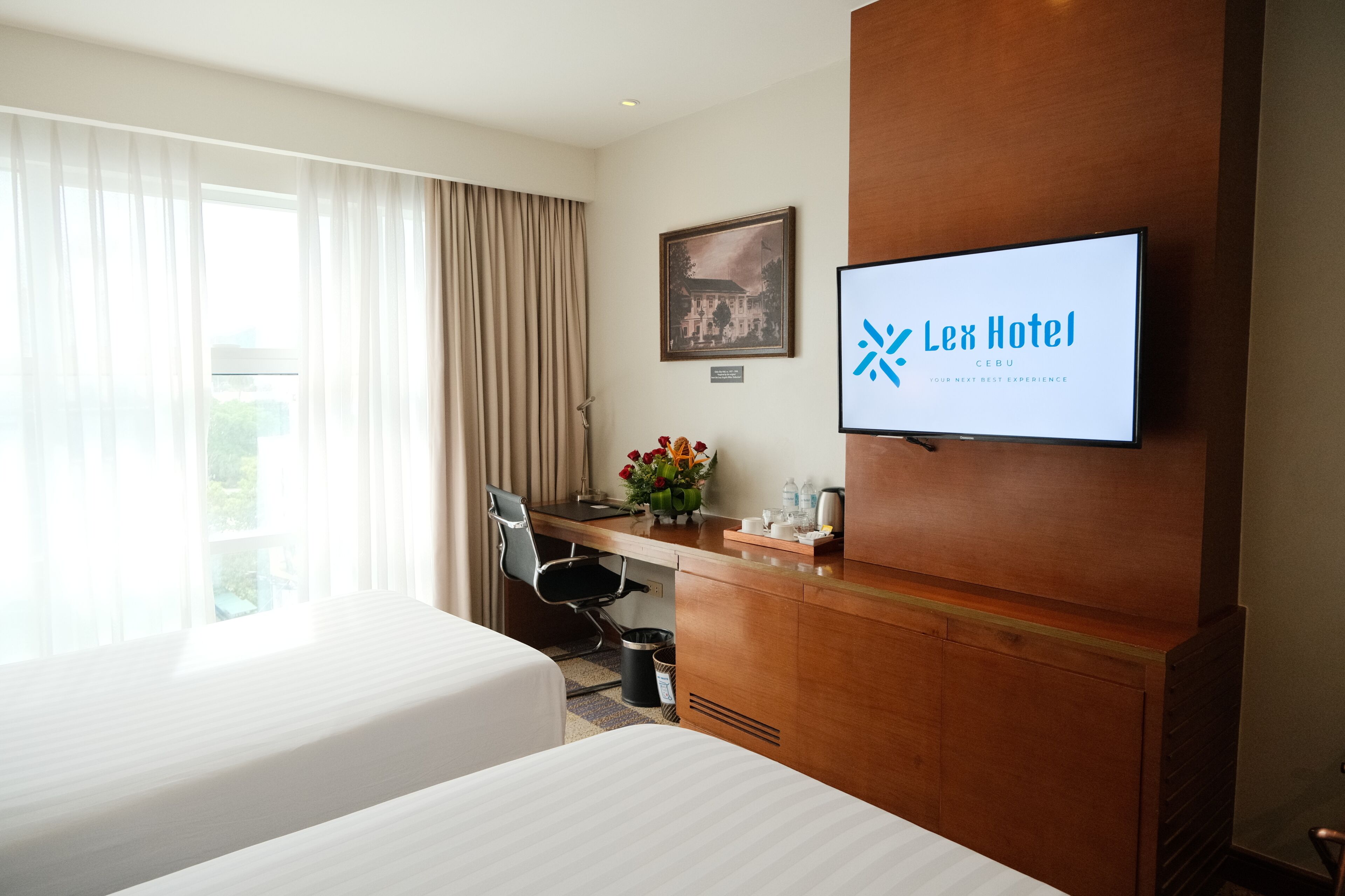 A hotel room with two beds, a desk, a chair, a TV, and a window with curtains.