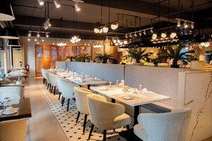 A restaurant with long tables, chairs, and hanging lights.