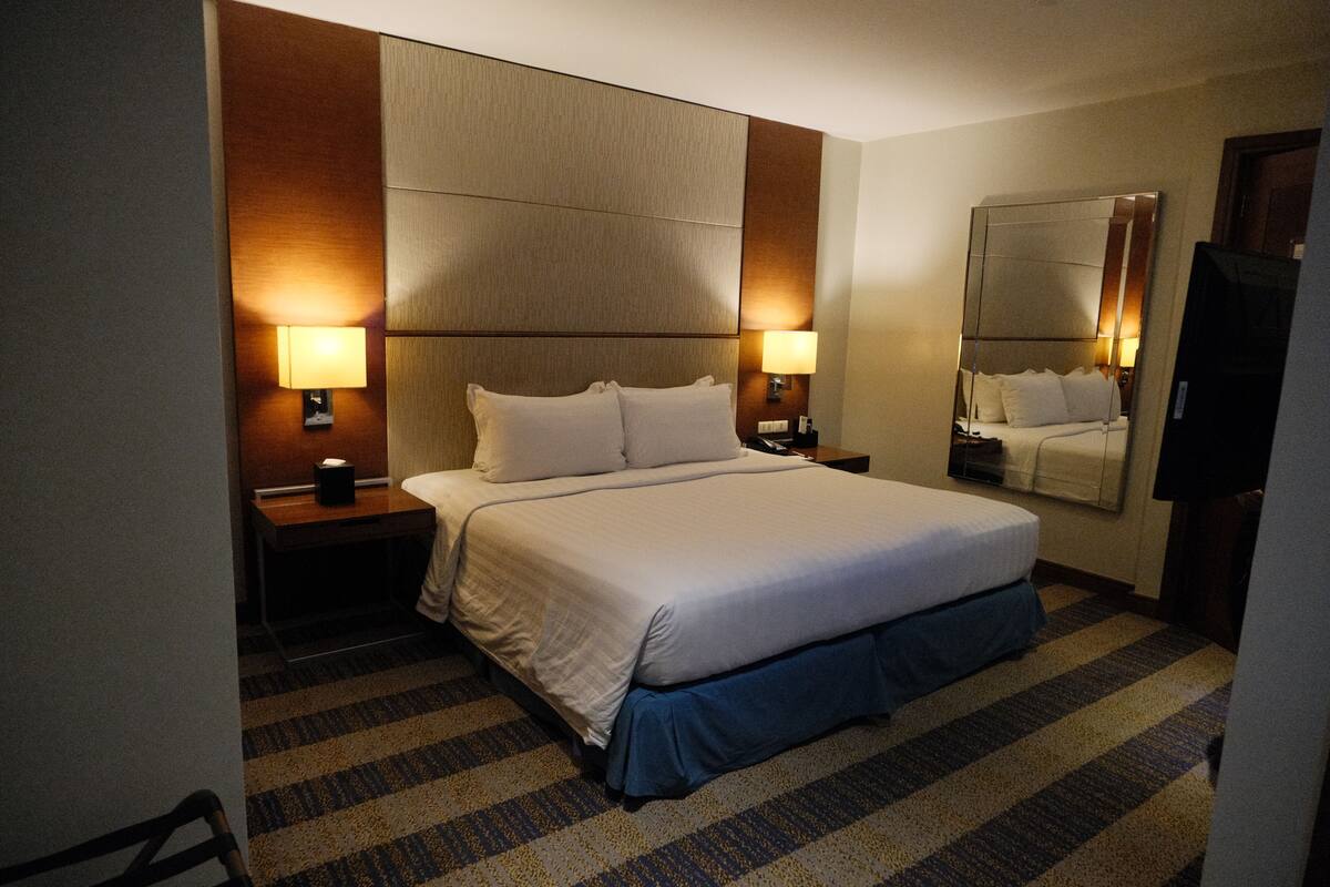 A hotel room with a large bed, two bedside tables, a mirror, and a television.