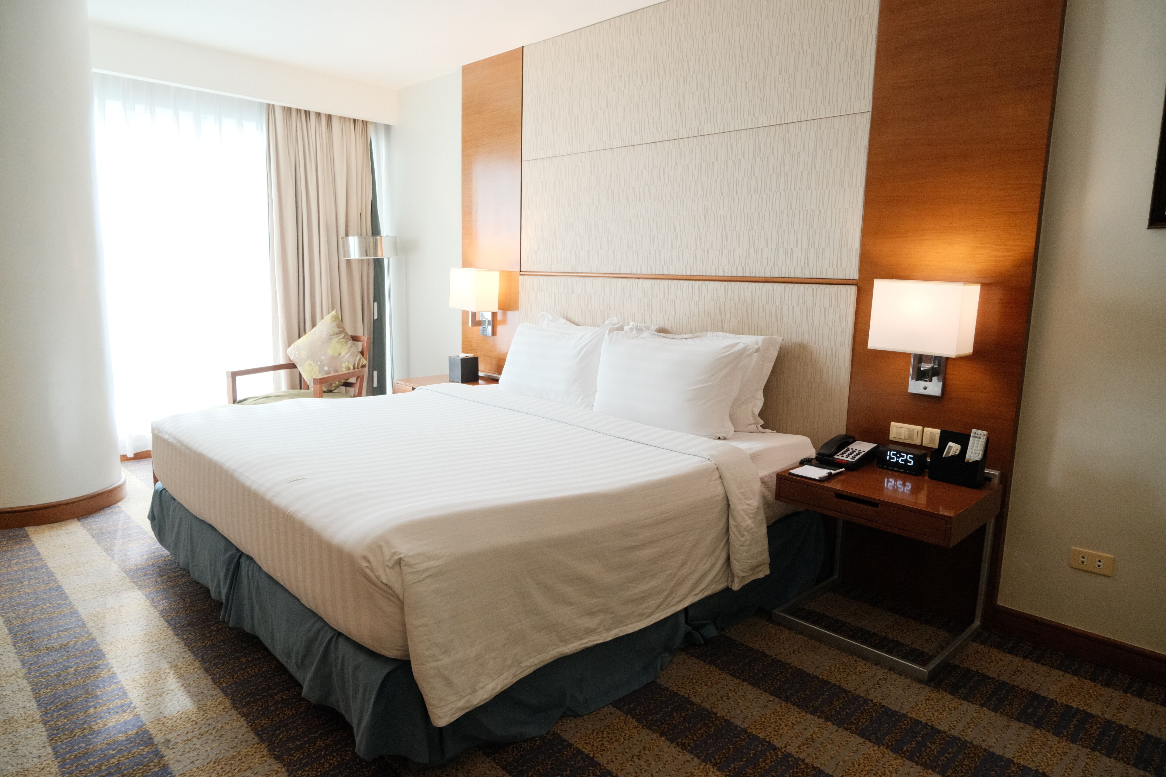 Habitación de hotel con una cama grande, lámparas de noche, un escritorio con teléfono y un reloj.
