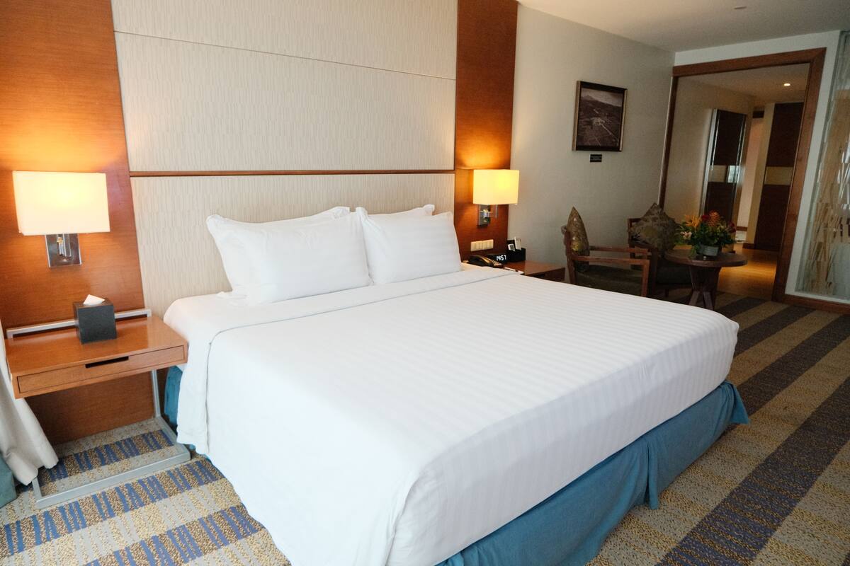 A hotel room with a large bed, bedside lamps, a nightstand, a chair, and a small table with a flower arrangement.
