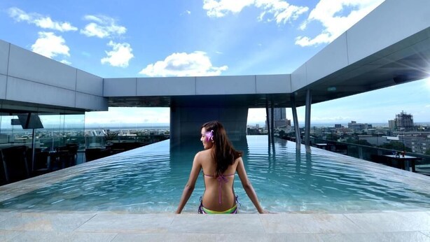 Una mujer con traje de baño en una piscina infinita en la azotea, con vista a la ciudad.