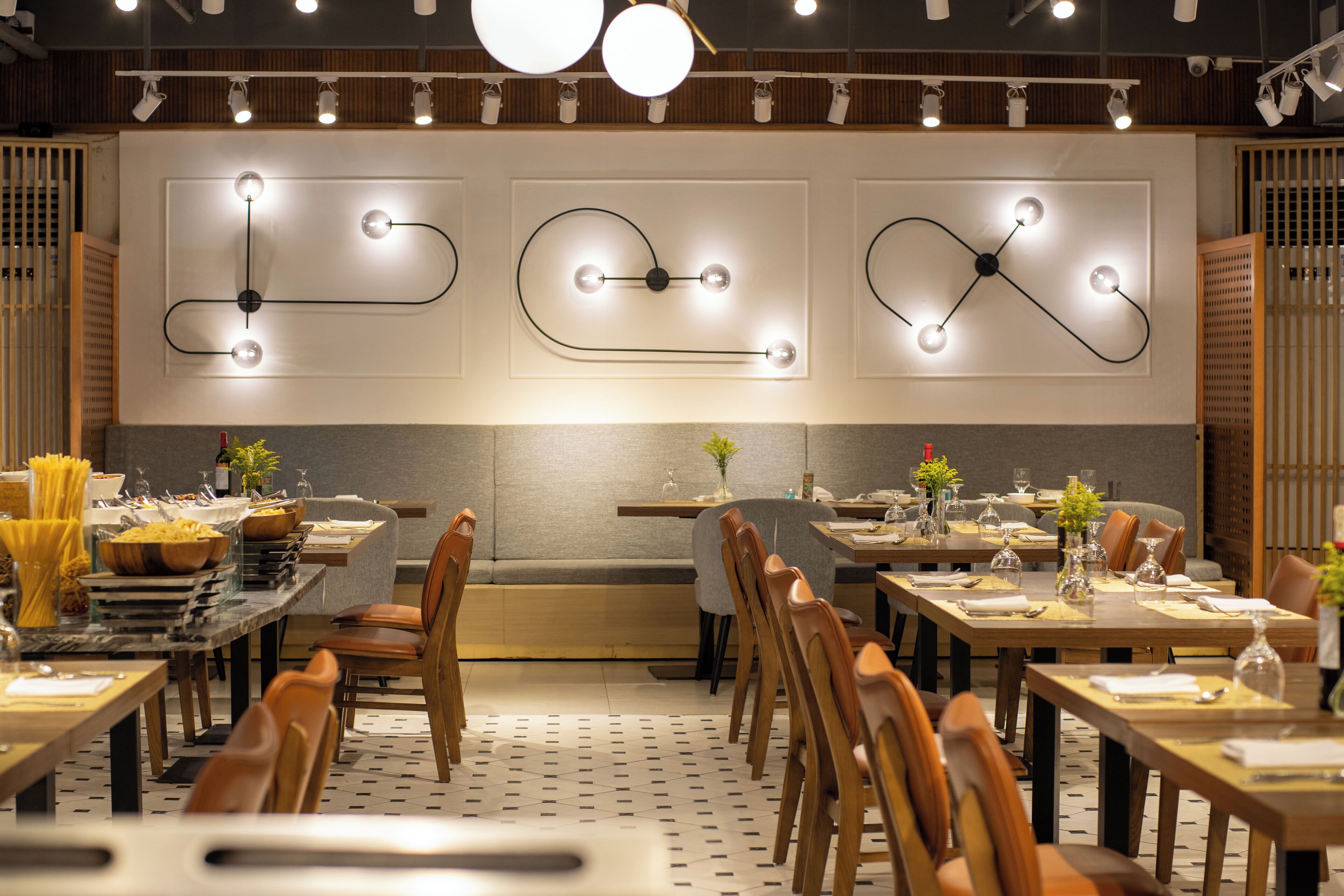A restaurant with multiple tables and chairs, modern light fixtures on the wall, and a patterned floor.