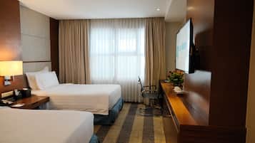 A hotel room with two beds, a desk with a chair, a television, and a window with curtains.