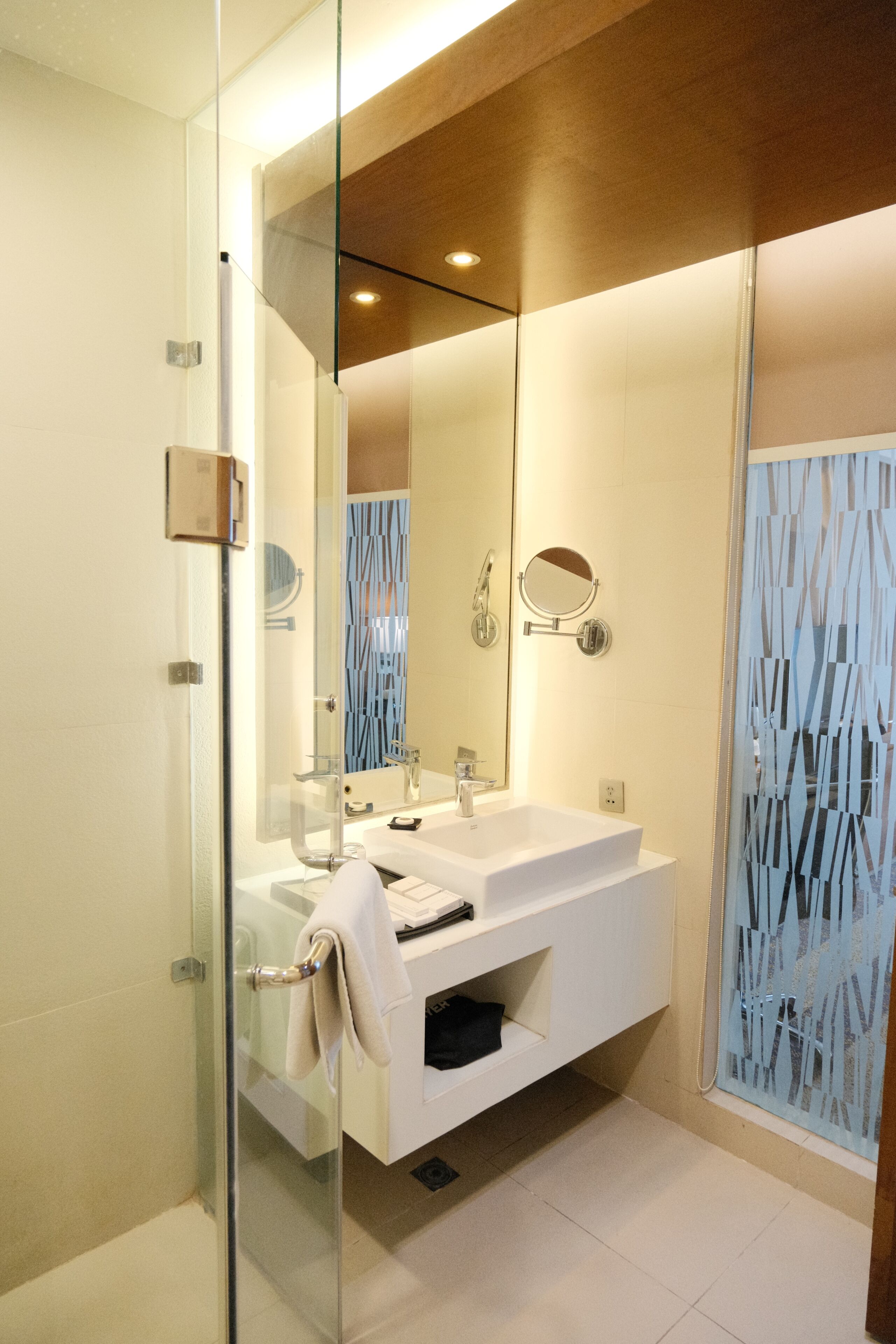 A modern bathroom with a glass shower enclosure, a white vanity with a mirror, and a patterned glass partition.