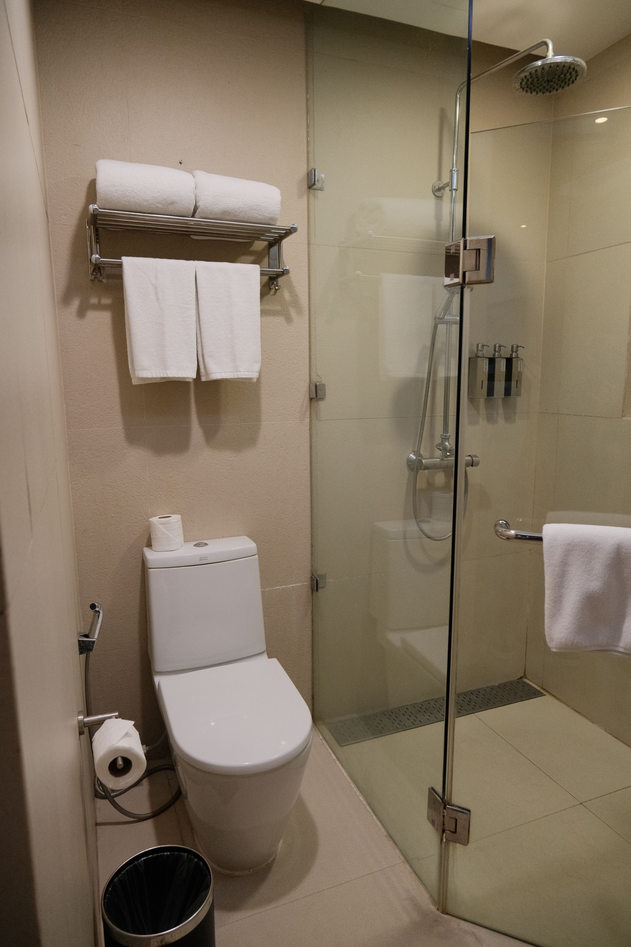 Ein Badezimmer mit Toilette, einer Duschkabine, einem Handtuchhalter und einem Mülleimer.