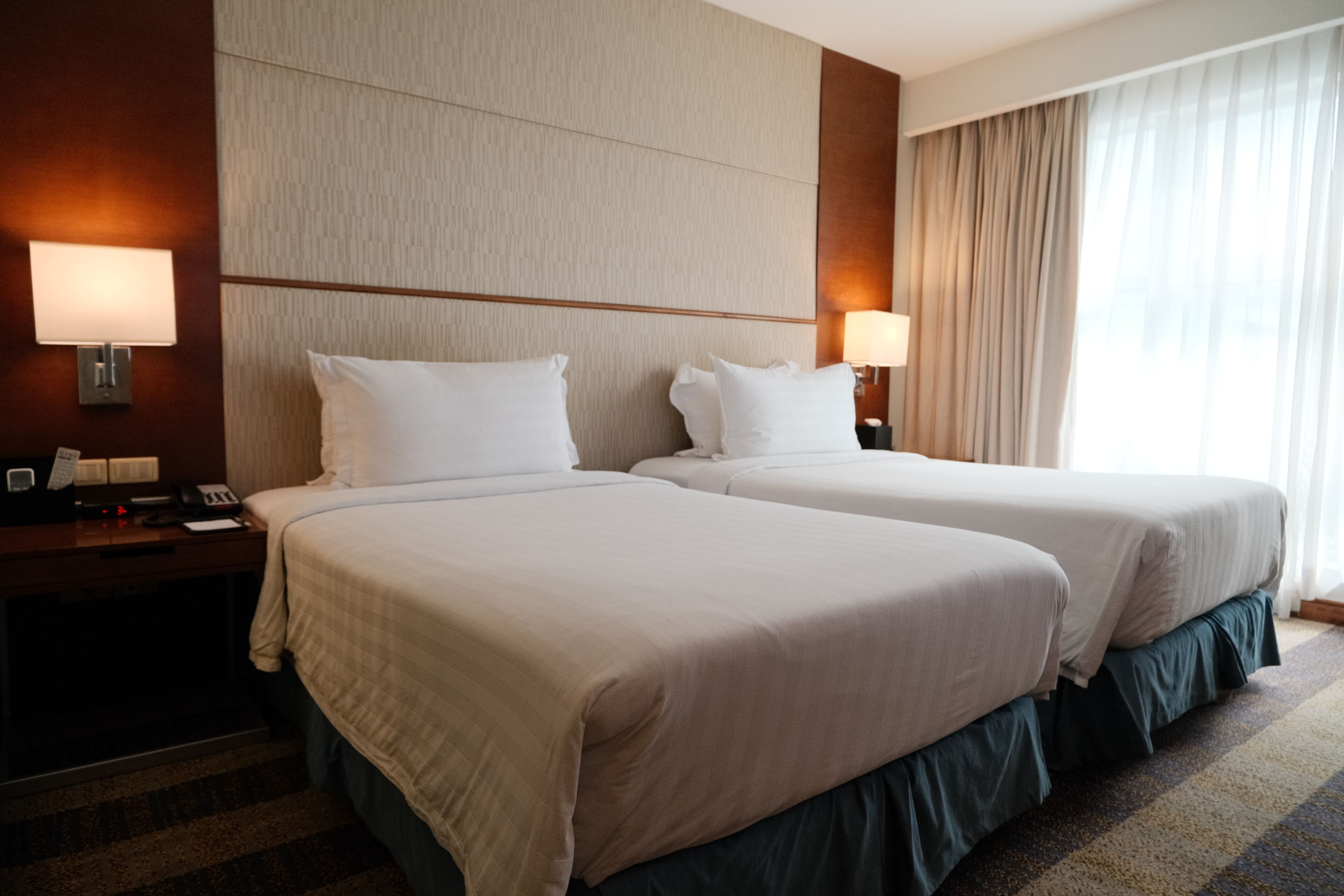 Habitación de hotel con dos camas, un escritorio con lámpara y una ventana con cortinas.