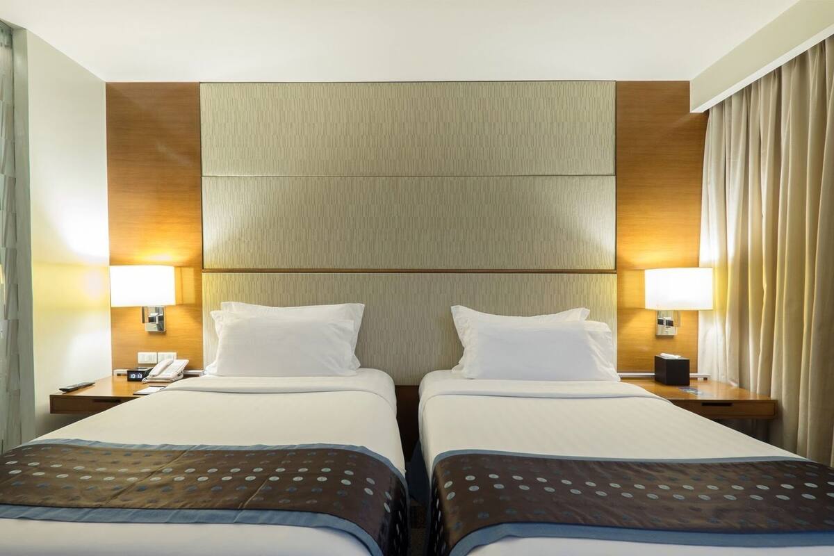 A hotel room with two beds, a wooden headboard, bedside lamps, a nightstand with a phone, and a window with curtains.