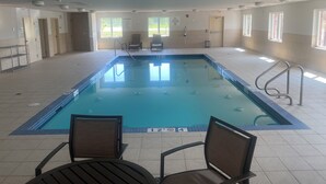 An indoor swimming pool with clear pool rules signs, a lifeguard chair, and a seating area with chairs.