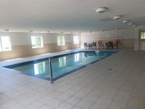 An indoor swimming pool with clear water, tiled floor, and ceiling-mounted lights.