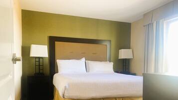 Habitación de hotel con una cama grande, dos mesitas de noche con lámparas, una pared verde y una ventana con cortinas.