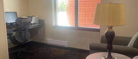 A hotel room with a desk, computer, office chair, sofa, and a lamp.