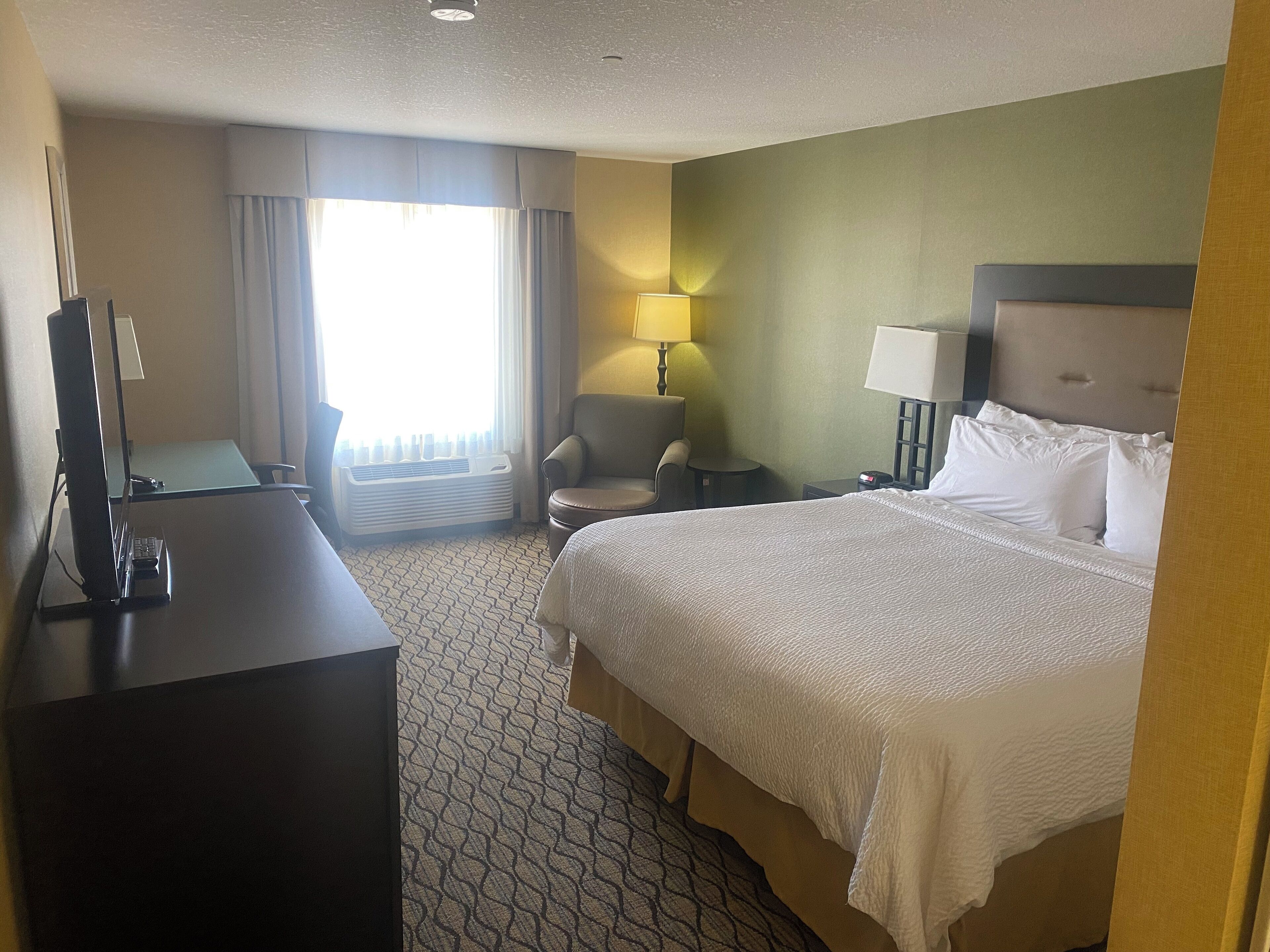 A hotel room with a bed, a desk, a chair, a lamp, and a window with curtains.