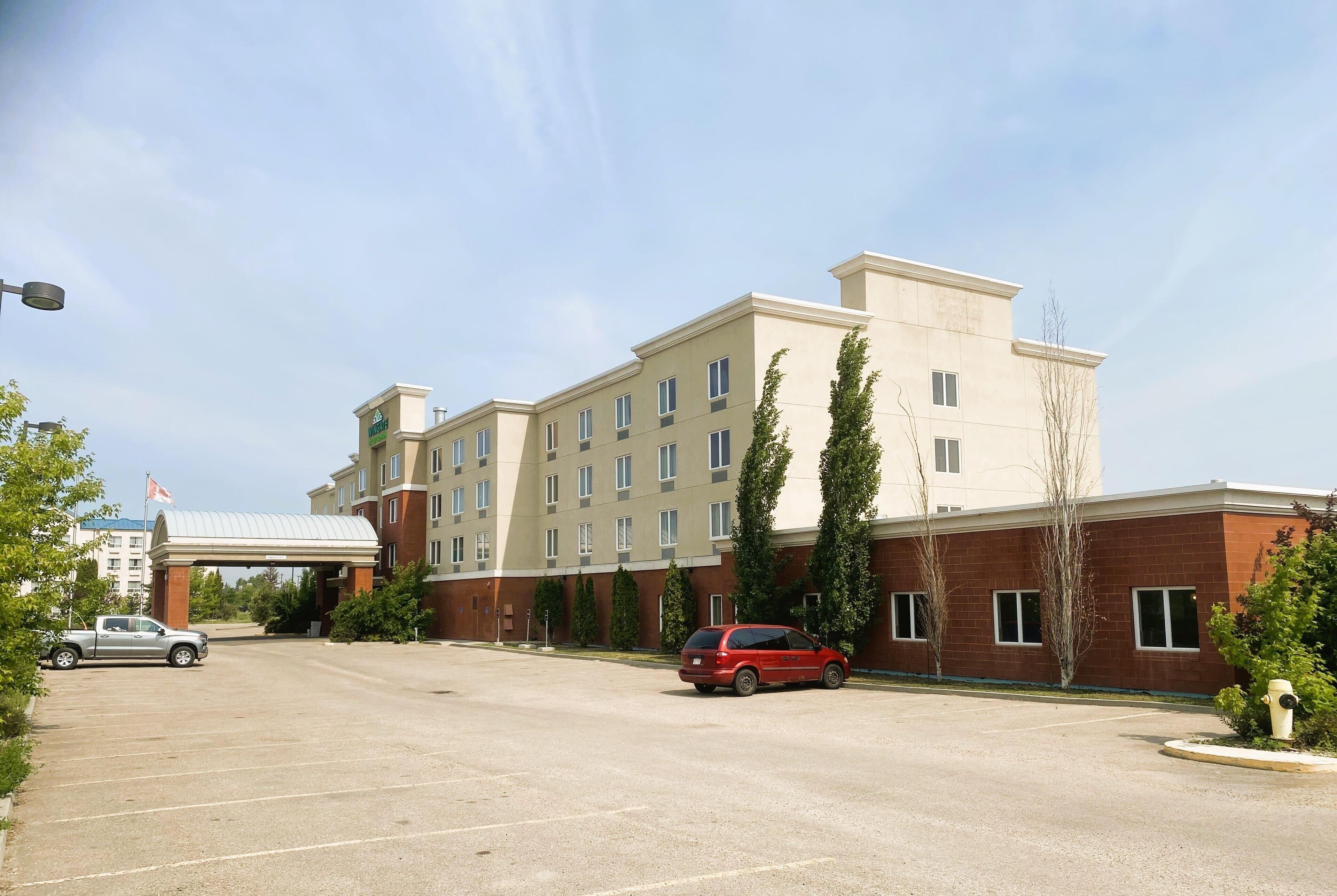 A hotel with a parking lot, a red car, and a building with multiple windows and a flat roof.