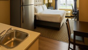 A hotel room with a bed, a refrigerator, a sink, a dining table, and a chair.